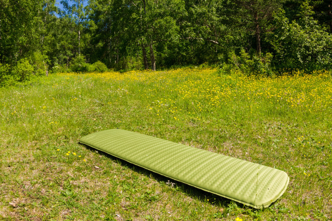 Green inflatable camping mattress on the green grass