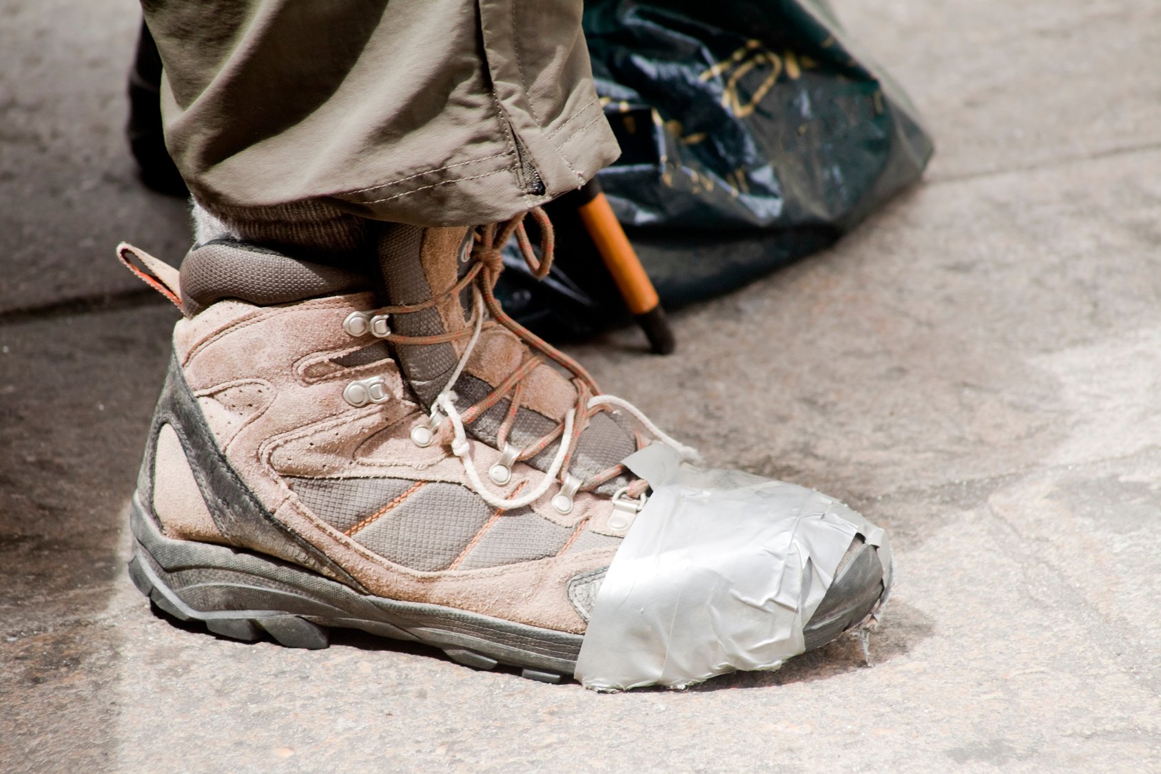 Pilgrim wearing broken hiking boot, repaired with adhesive tape